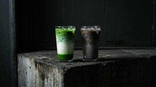 Matcha latte next to a coffee latte on a dark industrial surface